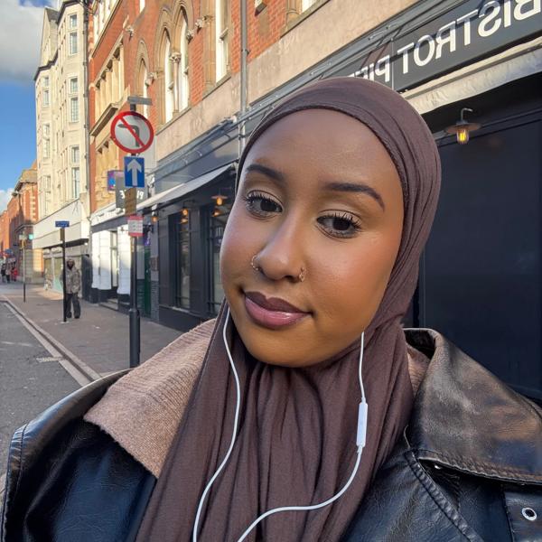 A young black woman wearing a hijab is stood outside and smiling