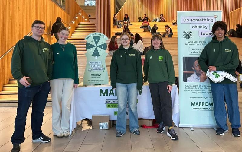 A photo of five young people wearing Anthony Nolan branded jumpers and stood in front of a donor recruitment stall at Warwick University.