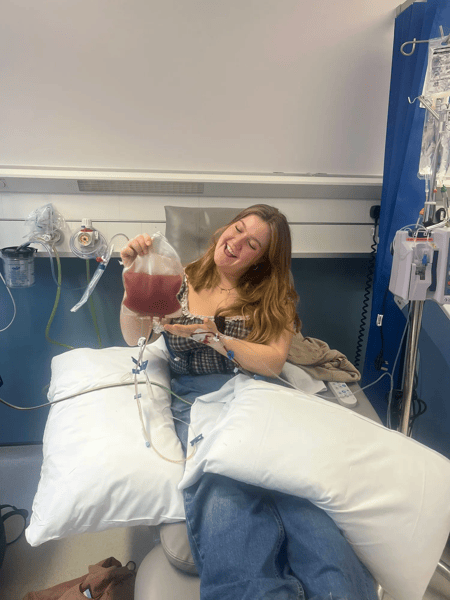 Edie, a Liverpool Marrow volunteer poses in hospital, smiling with her bag of stem cells after her donation. 