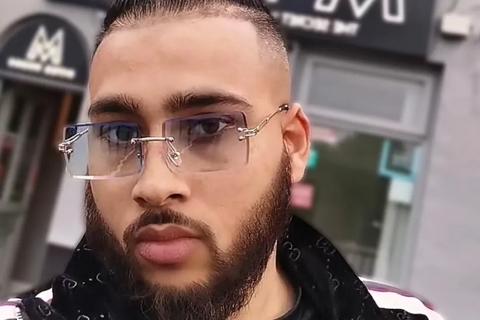 A young man with short black hair and a beard, wearing glasses