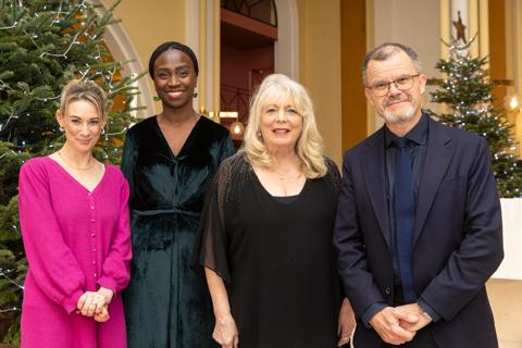 A group of 4 people smiling at the camera in front of 2 Christmas trees.