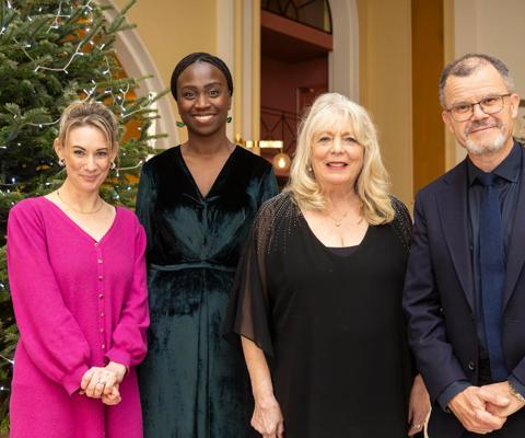 A group of 4 people smiling at the camera in front of 2 Christmas trees.