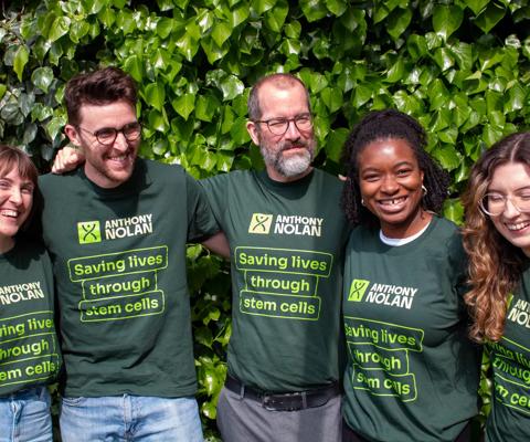 A group of men and women in Anthony Nolan tshirts with their arms around each other smiling and laughing