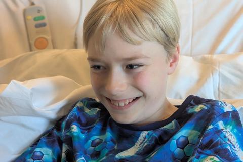 A boy lies in a hospital bed, smiling