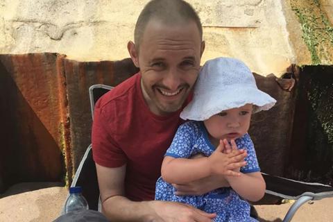 Alex, smiling at camera and holding his daughter.