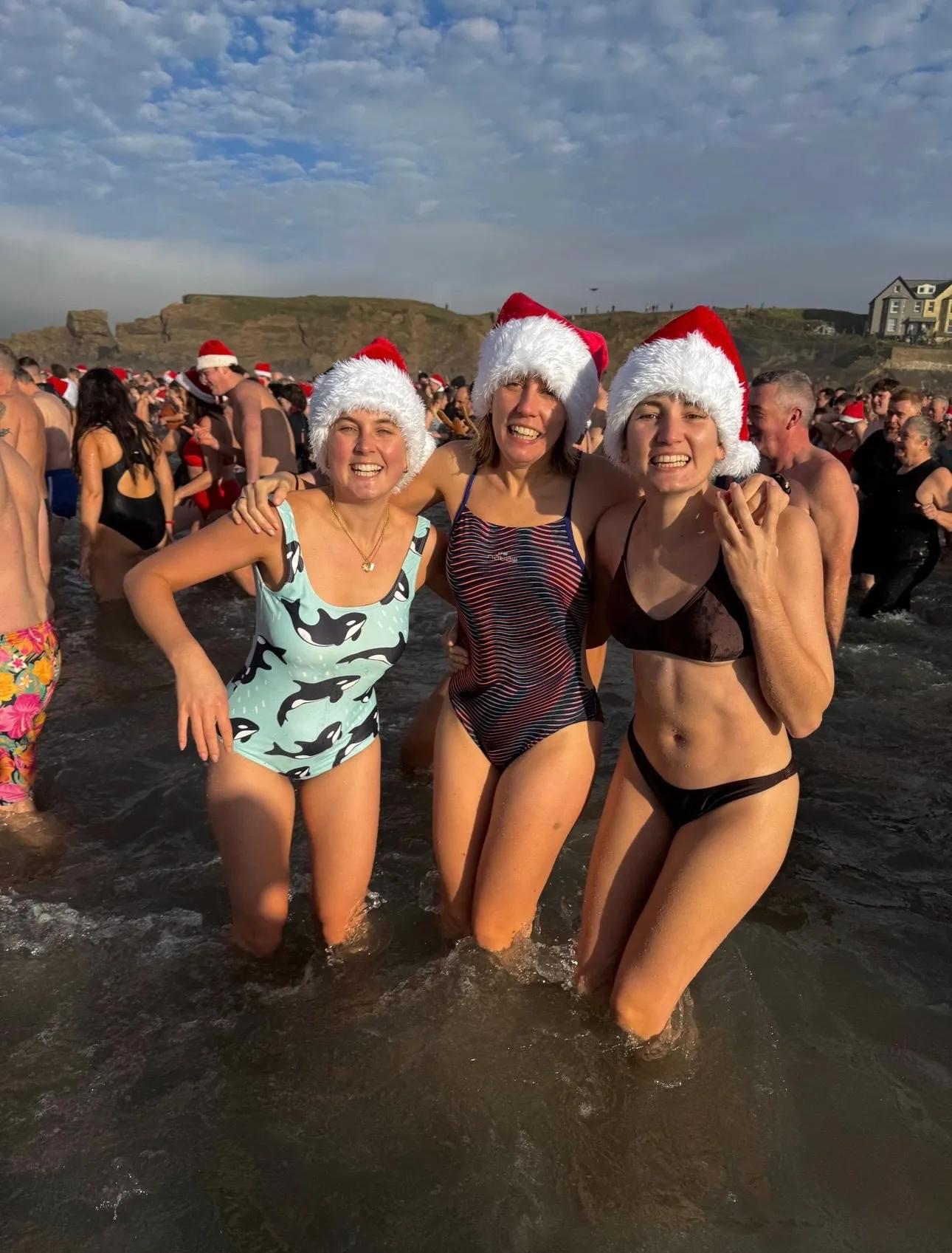three young women posing together in the sea wearing santa hats