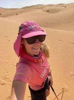 a woman wearing sunglasses smiling in front of sand dunes