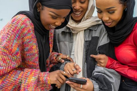 Three young Asian girls with headscarves on looking at a smartphone laughing and smiling