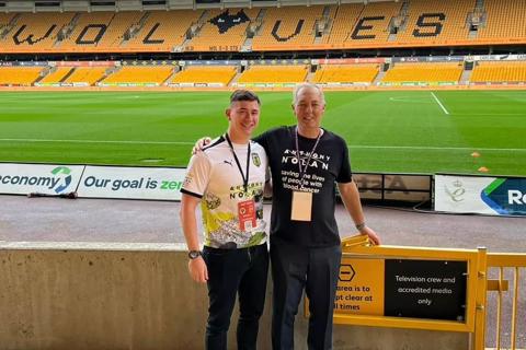 an older man and younger man at a football stadium, both are wearing Anthony Nolan t-shirts