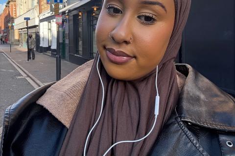 A young black woman wearing a hijab is stood outside and smiling