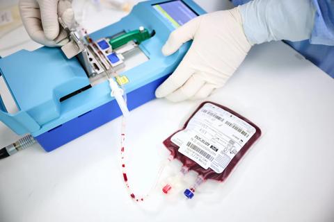 Blood sample bag with white label connected to blue machine on laboratory worktop.