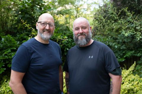 Two white middle-aged men stood together outside smiling at the camera