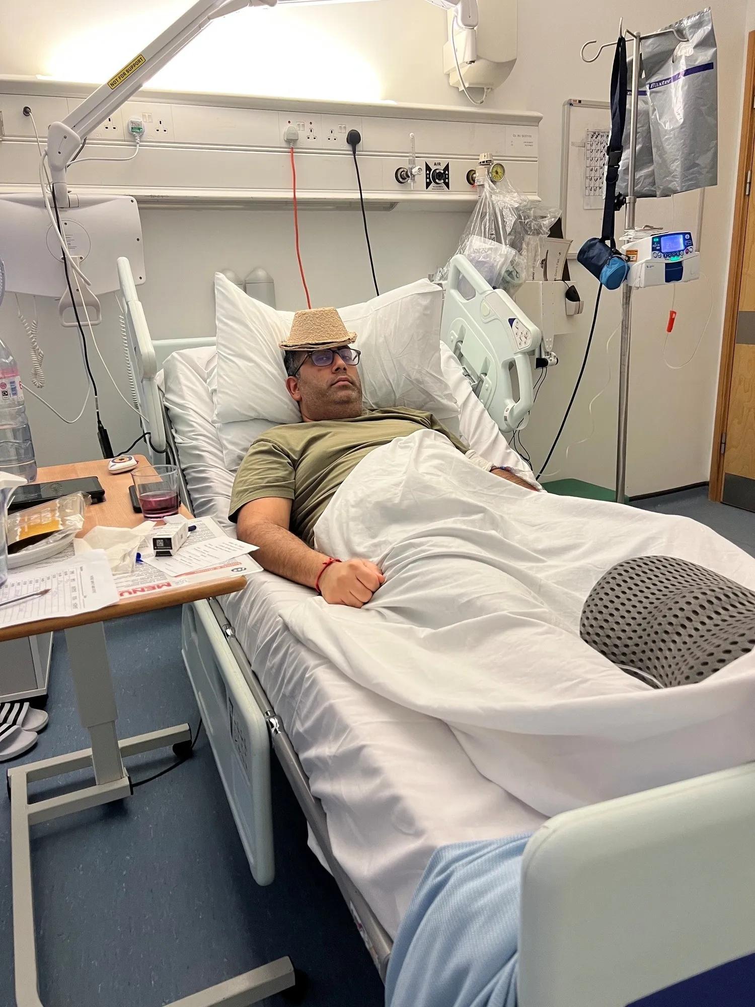 Neil  laying in a hospital bed wearing a cardboard bowl for a hat