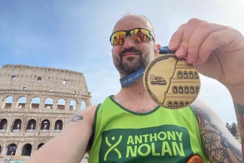 A man holding a medal in front of the colosseum in Rome in his Anthony Nolan running vest 
