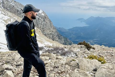 a young man on a rocky mountain gazing at the view, he's wearing all black