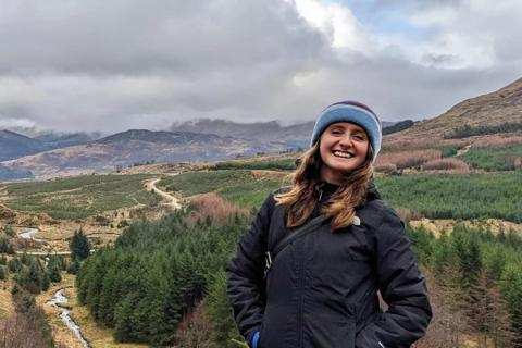 Natasha smiling in walking gear in a rugged outdoor landscape