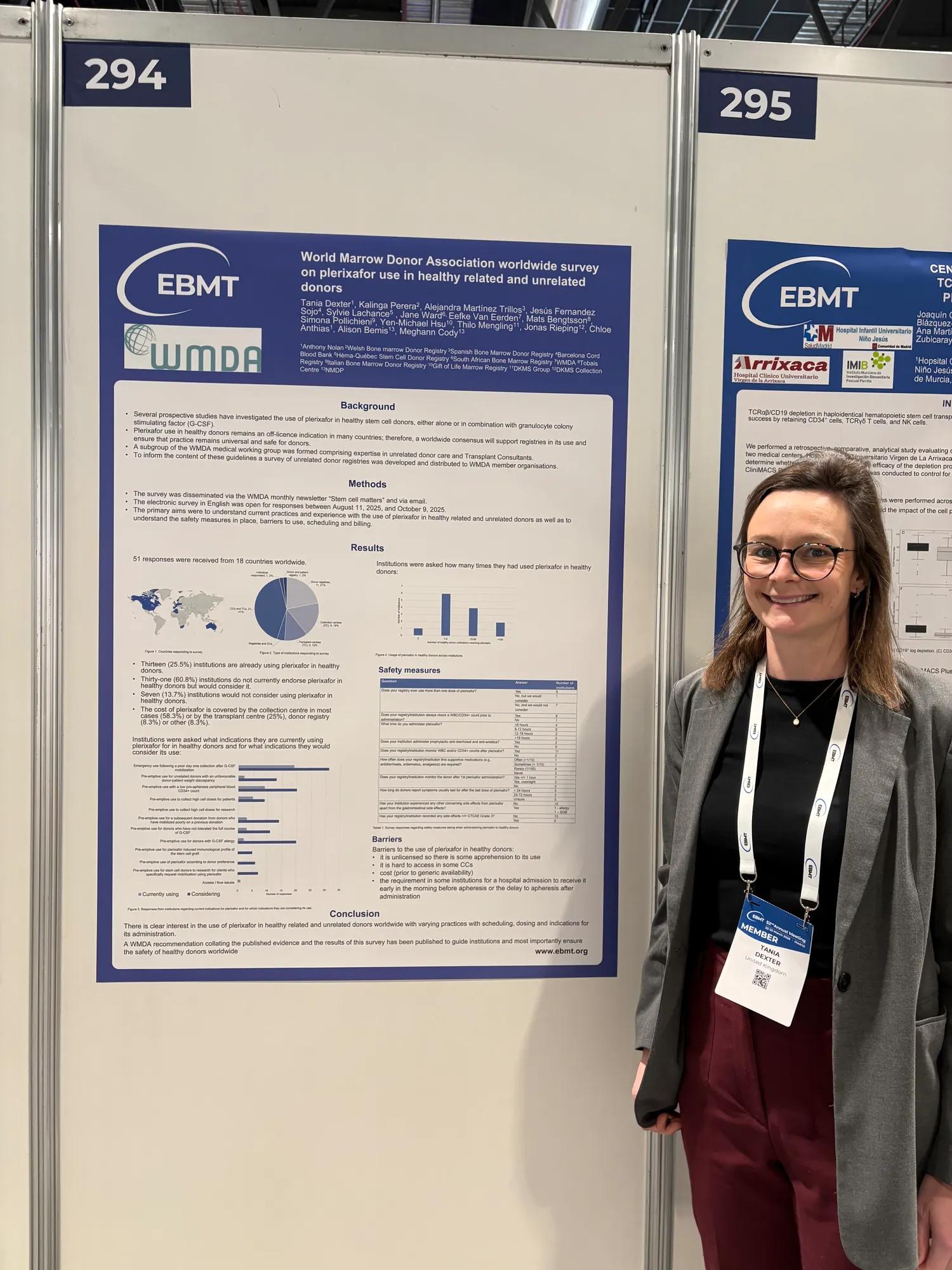 A smiling scientist stands next to a scientific poster at a conference