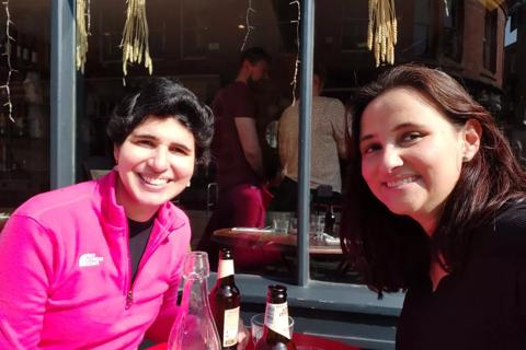 A brazilian woman with short hair sat at a table with another woman also brazilian, both smiling