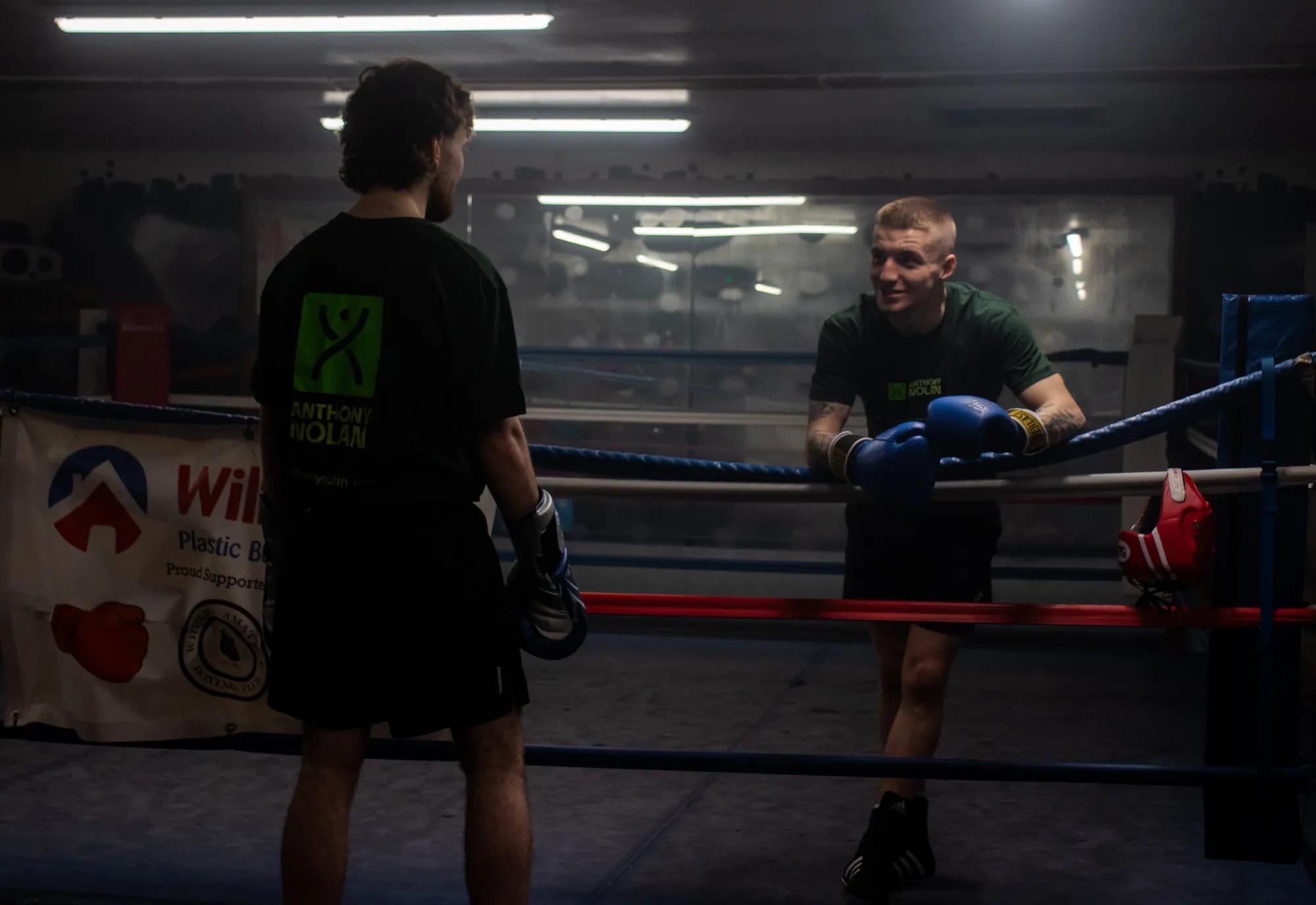 Two young men, named Reuben & Charlie, facing each other. Charlie is a boxing ring and Reuben is on the outside Apron, and they are looking at each other