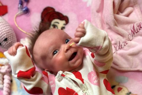 A photo of Dolcie-Mae smiling in a heart print baby grow