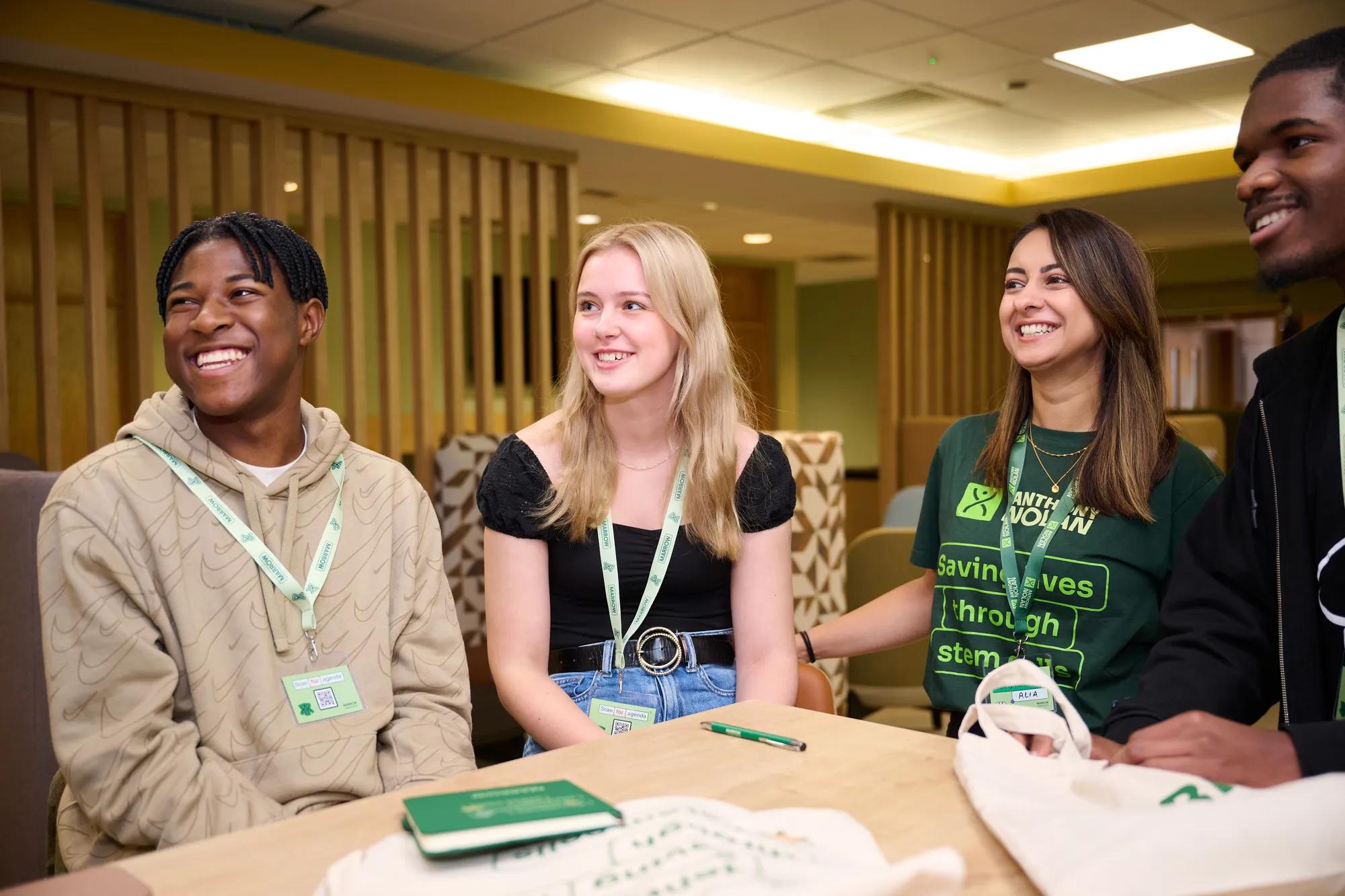 A photograph of four people sat around a table smiling and wearing Anthony Nolan lanyards