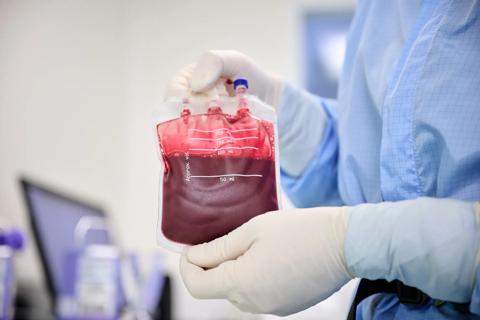 Blood sample bag held by scientist in blue coverall protective suit with gloved hands.