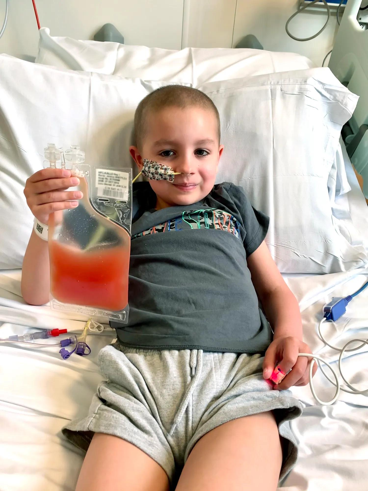 A little boy lying in a hospital bed holding up a bag of lifesaving stem cells
