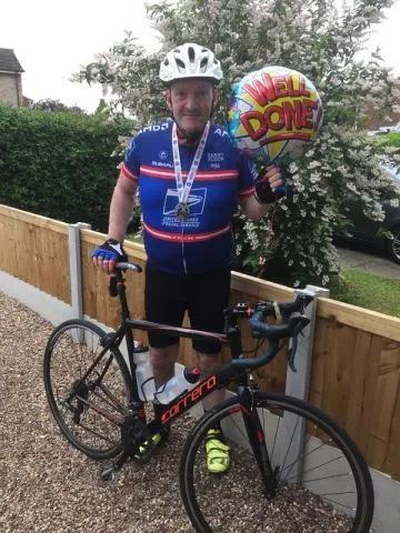 Scott standing by his bike holding a 'Well done' balloon