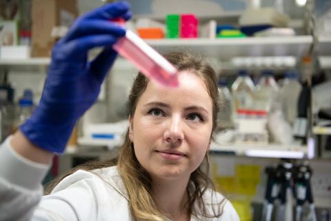 A person in a lab coat and wearing gloves looking at a tube