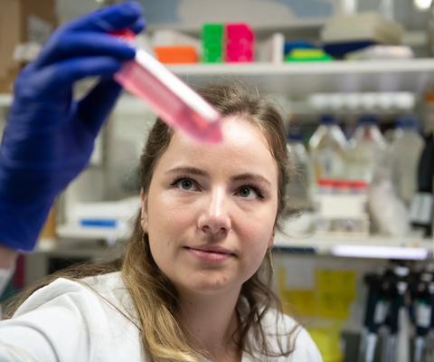 A person in a lab coat and wearing gloves looking at a tube