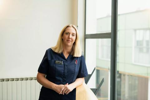 A headshot of a female nurse standing against a window