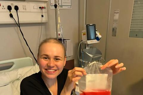 Faith sat in hospital bed smiling and holding a bag of stem cells