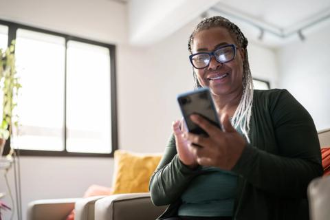 A middle-aged black woman sat on a sofa smiling and looking at her mobile phone