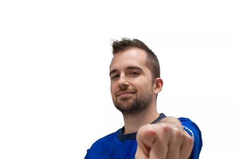 A man wearing the blue Everton Football Club home shirt. He is holding a yellow ball under his arm and pointing at the camera. 