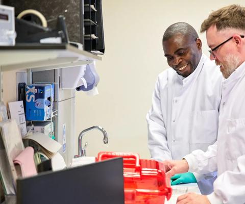 Two scientists stand at laboratory counter, opening red box with donated stem cells inside.