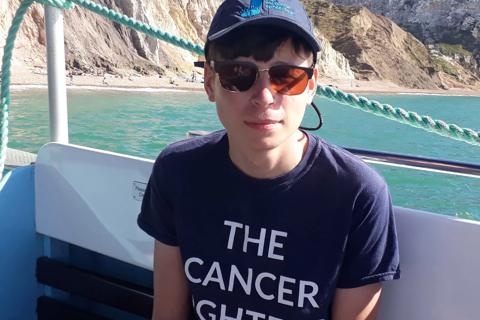 A young man wearing a cap and sunglasses. His t-shirt reads: the cancer fighters