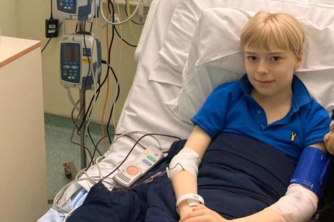 A boy lies in a hospital bed, in his arm is an IV