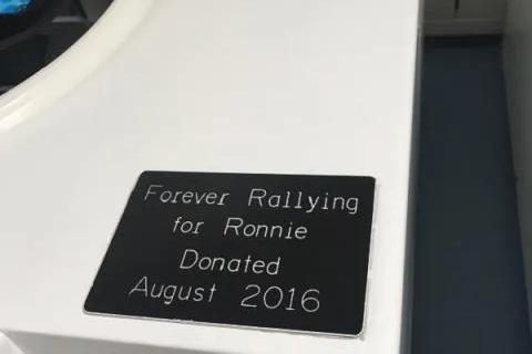 A corner of a centrifuge with a small black plaque reading 'Forever Rallying for Ronnie. Donated August 2016' 