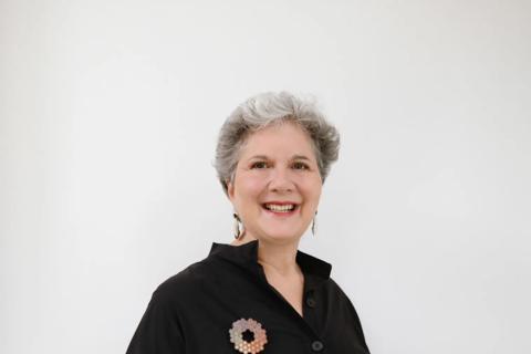 photo of Louise -  a woman standing in front of a white background, she's wearing a black dress and has short grey hair