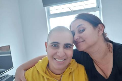 A brazilian woman with shaved hair with another woman also brazilian with her arm around her