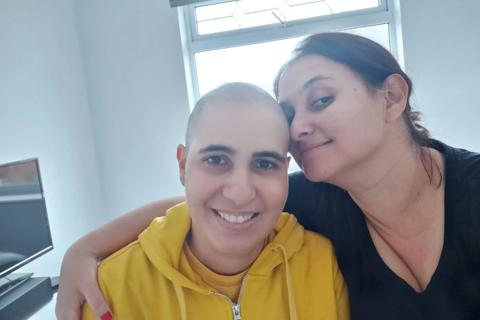 A brazilian woman with shaved hair with another woman also brazilian with her arm around her