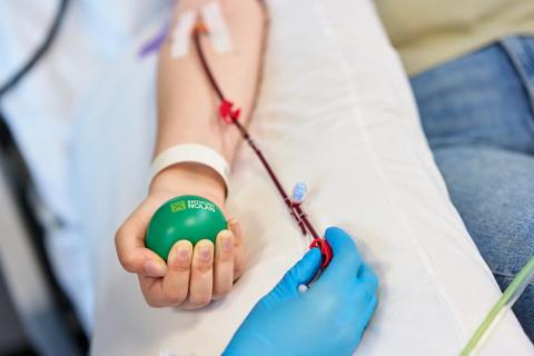 Donors sits on hospital bed with line in arm while holding green stress ball.