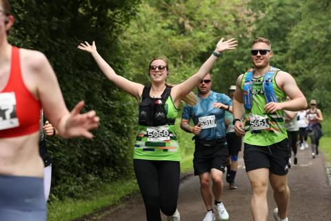 Runner in an Anthony Nolan running vest with her arms in the air smiling