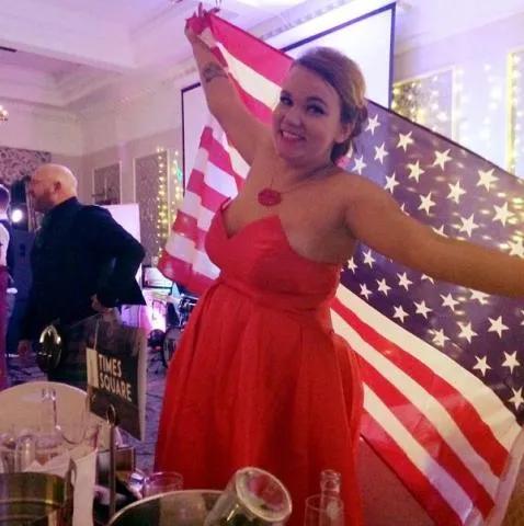 Amanda in  a red dress holding a big USA flag behind her