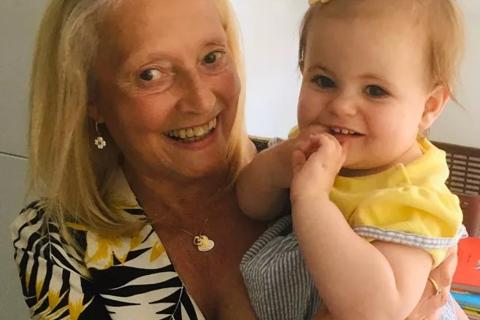 a woman smiling holding her baby granddaughter