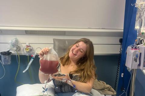 Edie, a Liverpool Marrow volunteer poses in hospital, smiling with her bag of stem cells after her donation. 