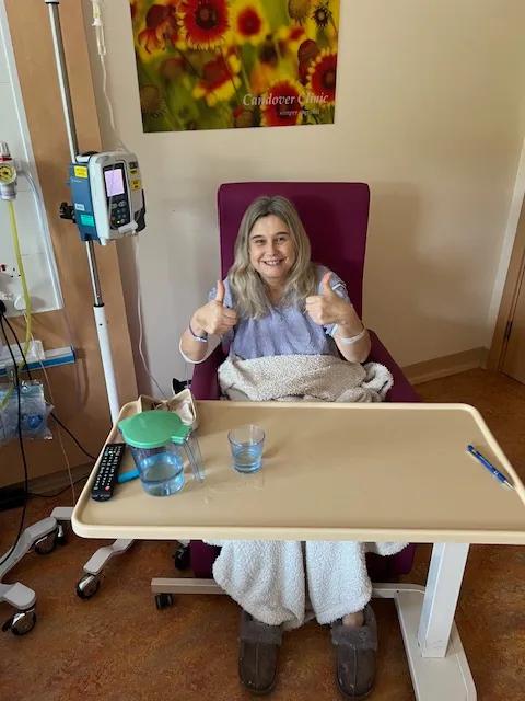 a woman with long blond hair sitting in a hospital chair hooked up to a drip