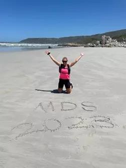 a woman on a beach raising her arms with MDS 2023 written in the sand