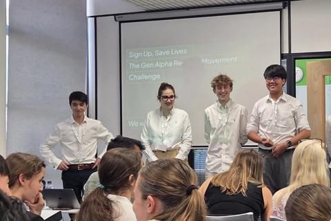 4 young people in white shirts stand in front of a large screen in entrepreneurs in action workshop