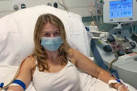 A young woman in a hospital bed with a covid mask on